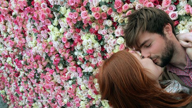 A couple kisses in front of a wall of roses