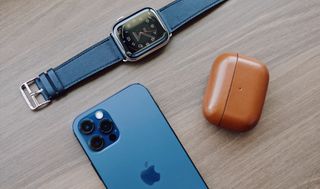 En Apple Watch, AirPods och en iPhone ligger bredvid varandra på ett träbord.