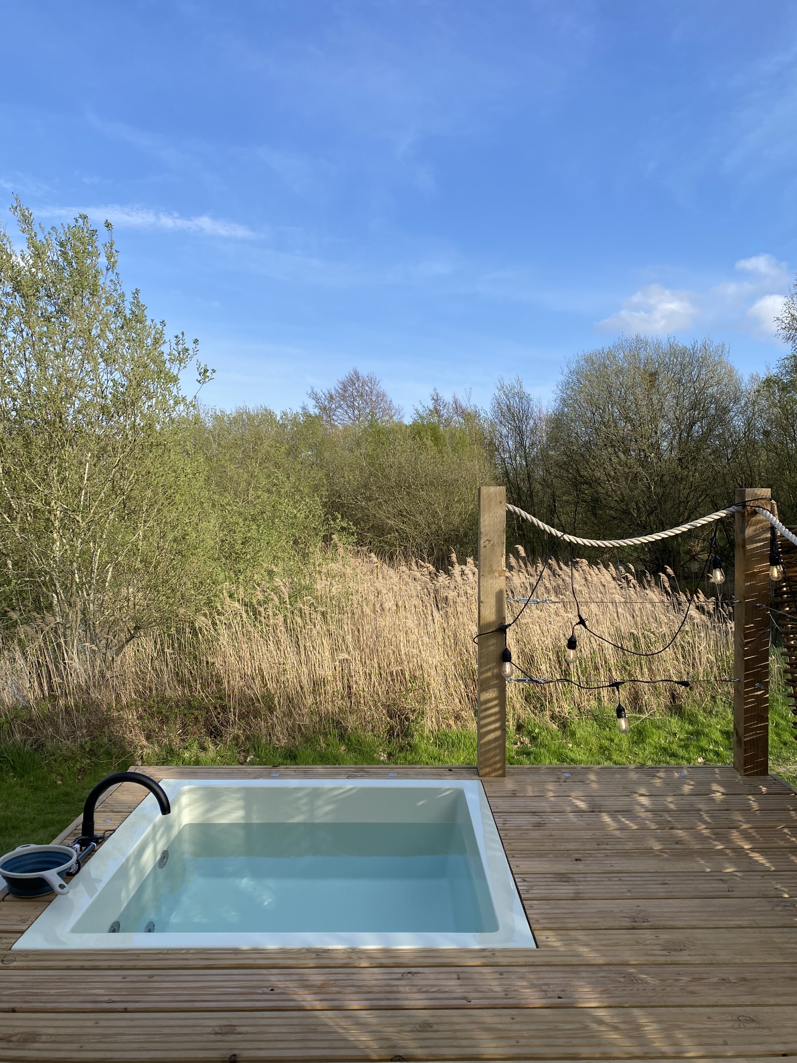 Small plunge pool built into some wooden decking with long grass in the background