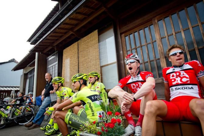 Riders wait for the start of stage 2 in front of an old Japanese house