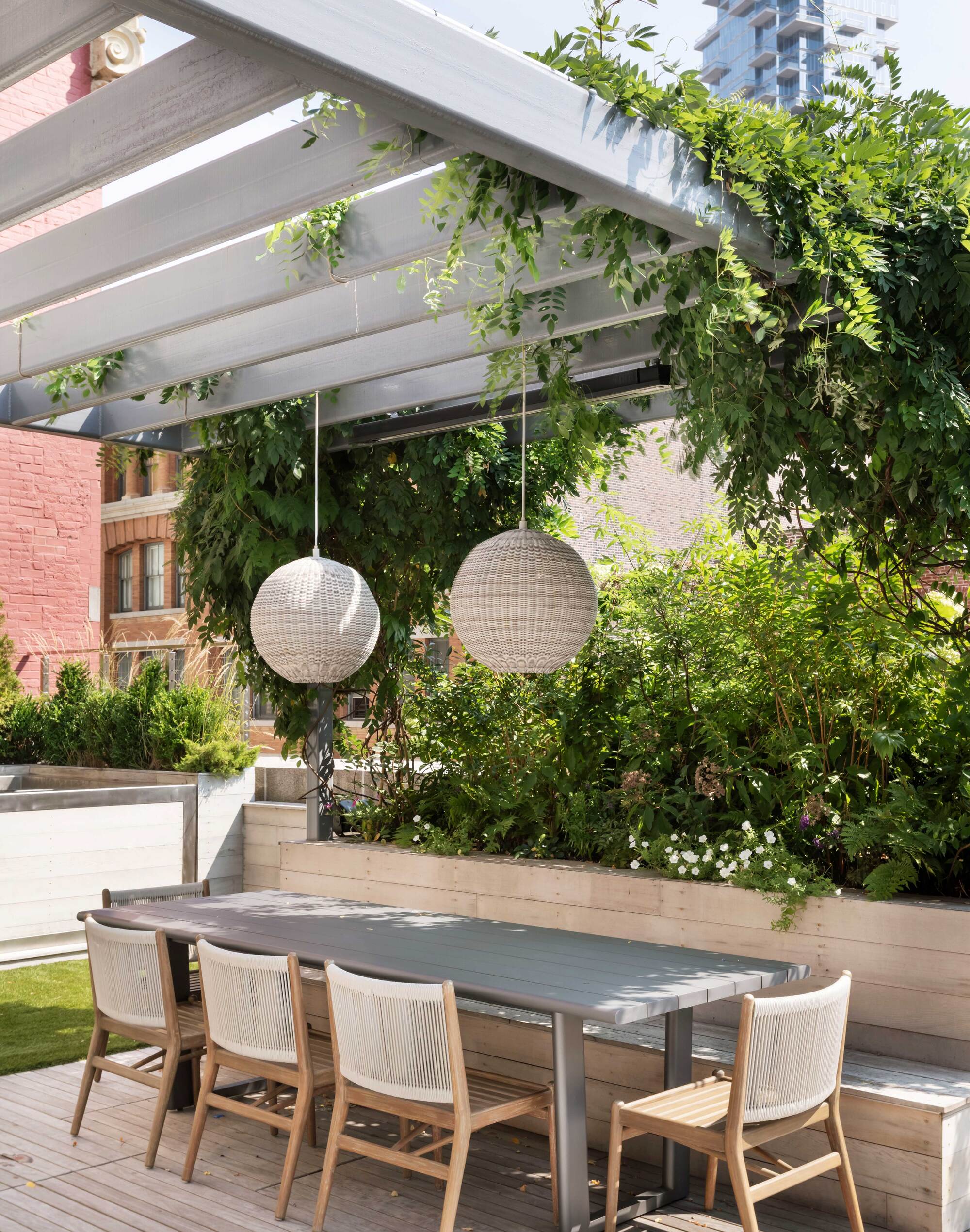 outdoor dining area with pergola, lanterns, plants growing up it, long dining tables, dining chairs, and a built-in bench seat running along one side
