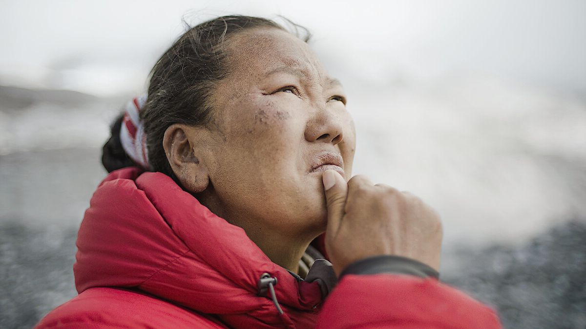 A still from the documentary Mountain Queen, one of the best Netflix documentaries, showing Lhakpa Sherpa looking off camera pensively, wearing a red coat.