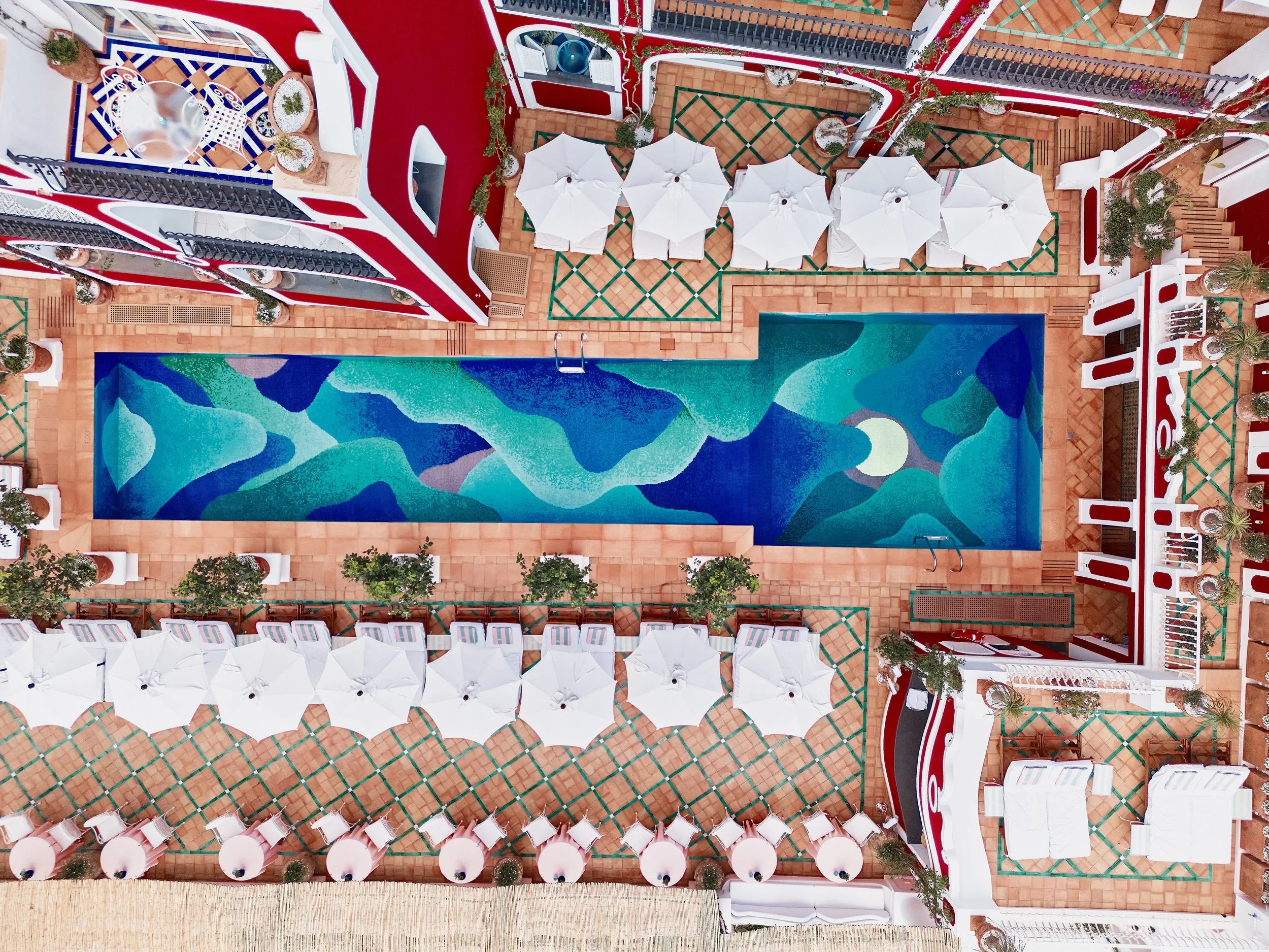 Aerial views of a colorful, vibrant pool with a bed made up of tiled waves in tones ranging from dark blue to green.