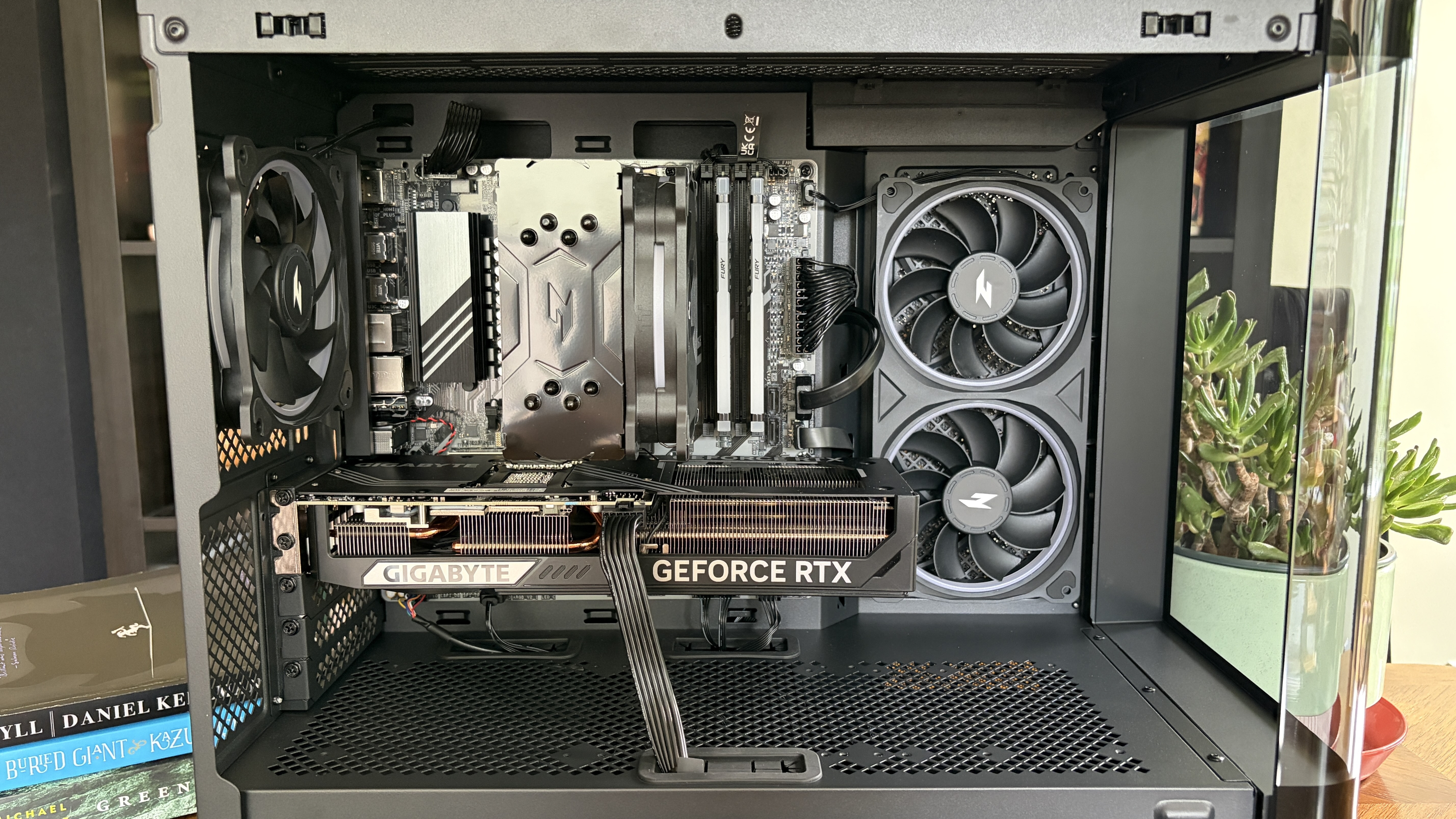 Interior view of a Nitro 65 computer case featuring a GIGABYTE GEFORCE RTX graphics card, cooling fans, and a motherboard, with books and a small plant in the background.