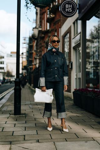 A woman wearing dropped wide-leg jeans, a denim jacket, white heels, and a hair scarf