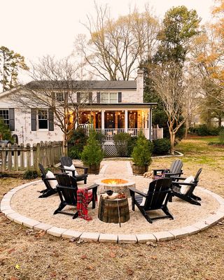 A fire pit with Adirondack chairs in a large unpaved backyard patio