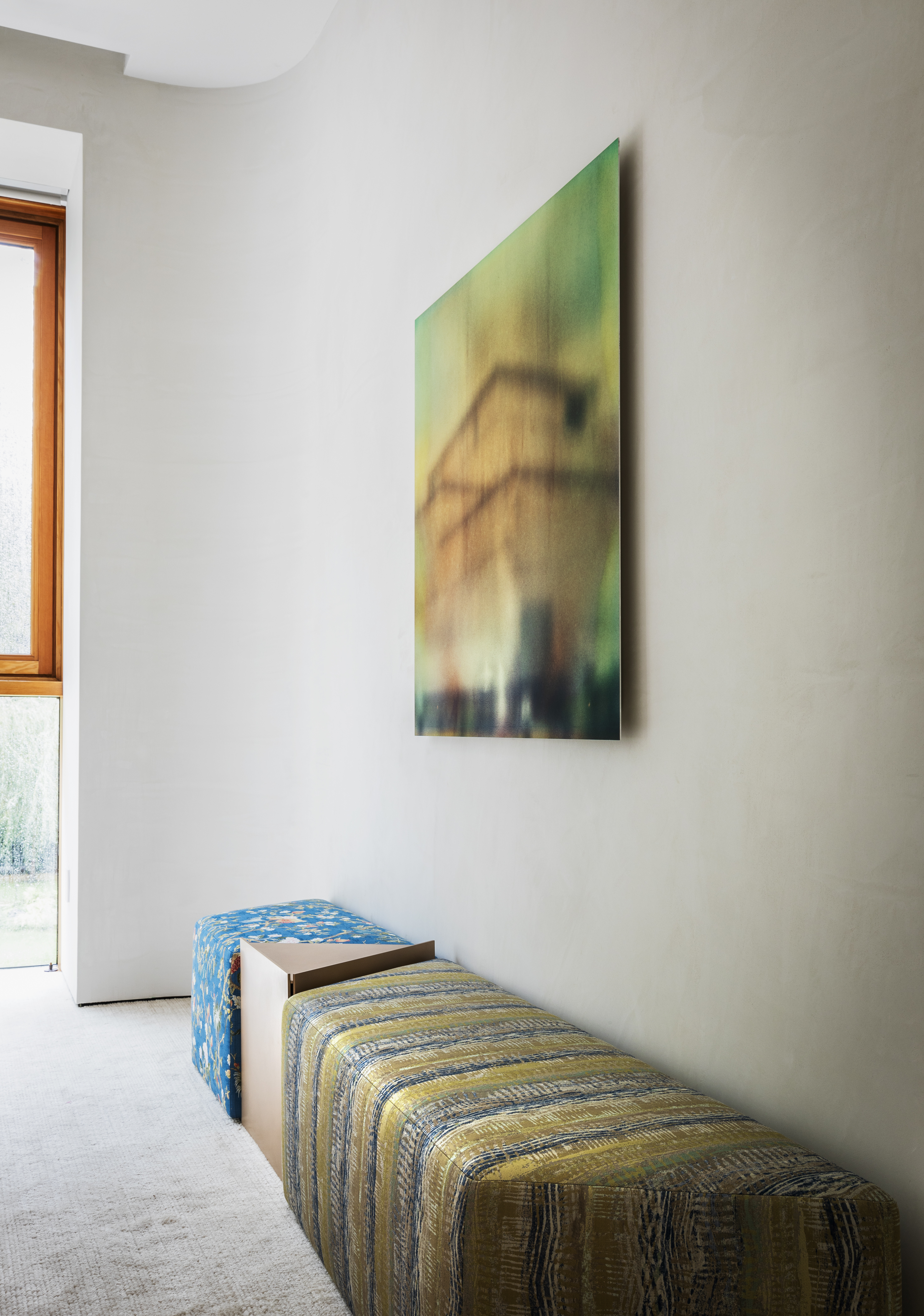 A cushioned bench with mixed fabrics and materials beneath a hanging artwork