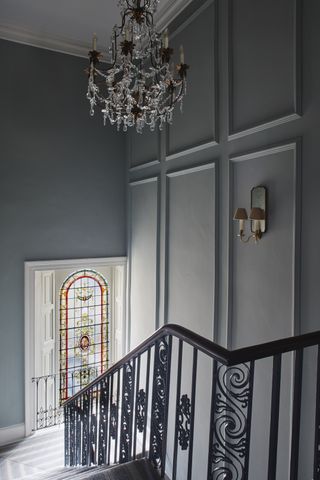 Staircase with ornate spindles, stained glass landing window, chandelier above and wall light