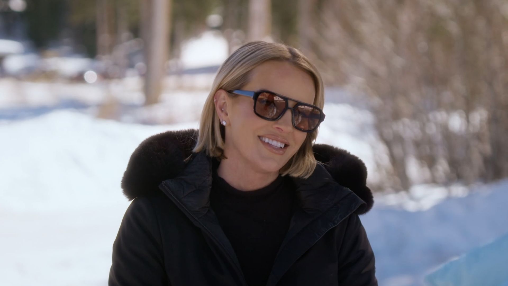 Whitney Rose smiling in a black coat and sunglasses talking to Lisa Barlow on RHOSLC.