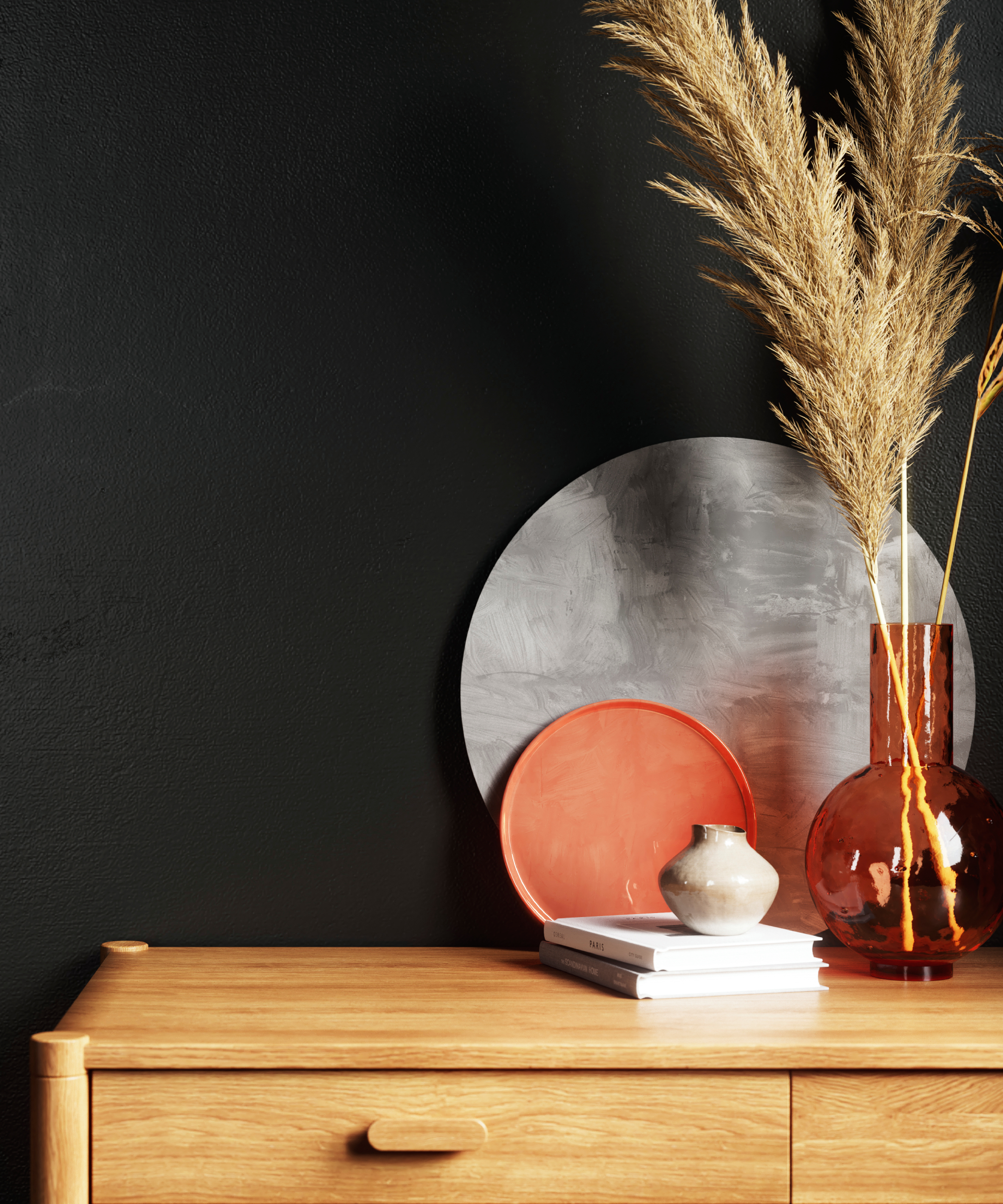 black wall, wooden chest of drawers and various decorative items on top including vase, dried grasses and books
