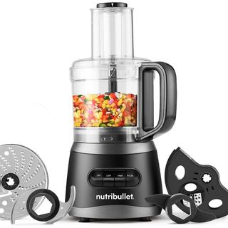 A Nutribullet 7 Cup Food Processor filled with vegetables ready to chop. Next to it are its other attachments and blades