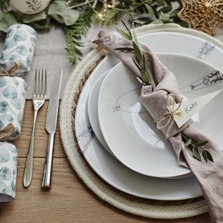 A dining table set for Christmas dinner with a pink linen napkin tied into a knot and placed on top of the plates