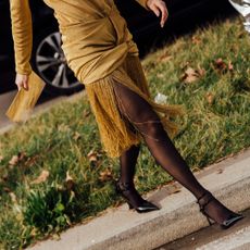 Woman's legs wearing a gold fringe dress, black tights, and black heels