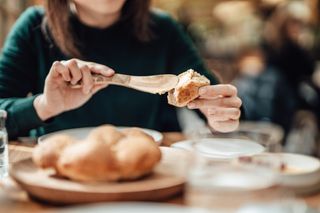 Close-up shot of a young woman spreading butter on some fresh bread with a wooden butter knife, enjoying lunch at the restaurant. Healthy eating with whole-grain concept.