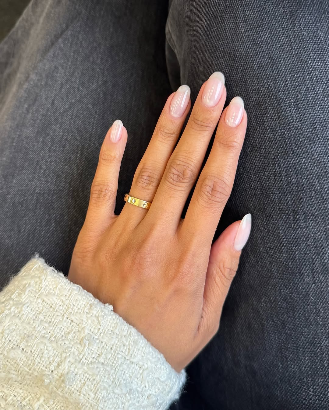 Close-up photo of a hand showcasing almond-shaped nails painted in pale pink with a chrome finish.