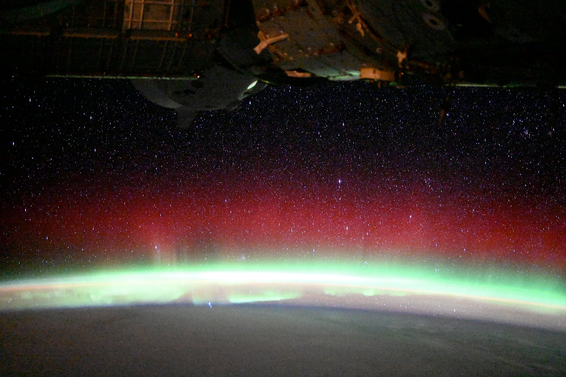 a white, green and red glow emanates from a planet as a space station orbits overhead