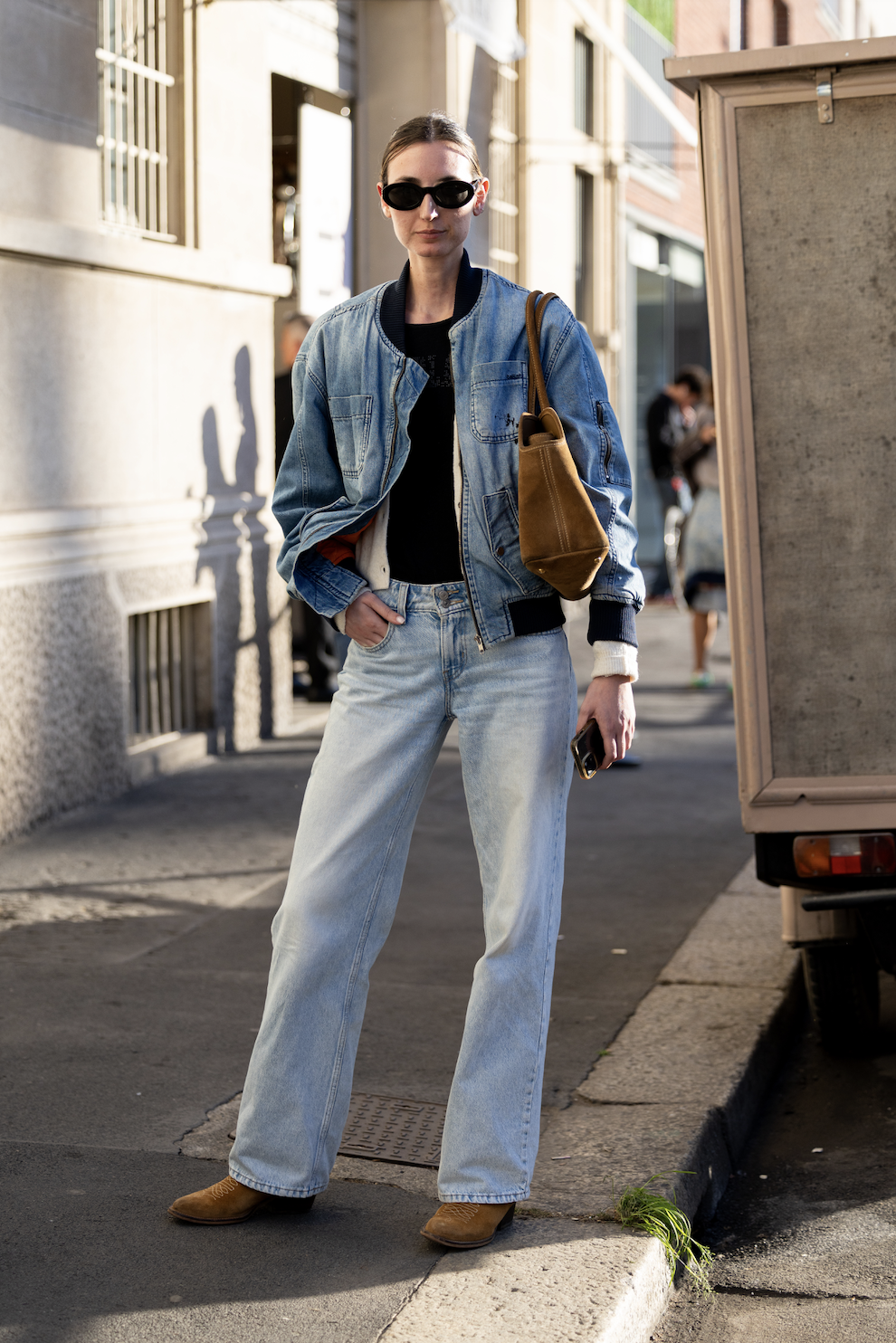A woman wears a denim jacket, light-wash jeans and brown boots.
