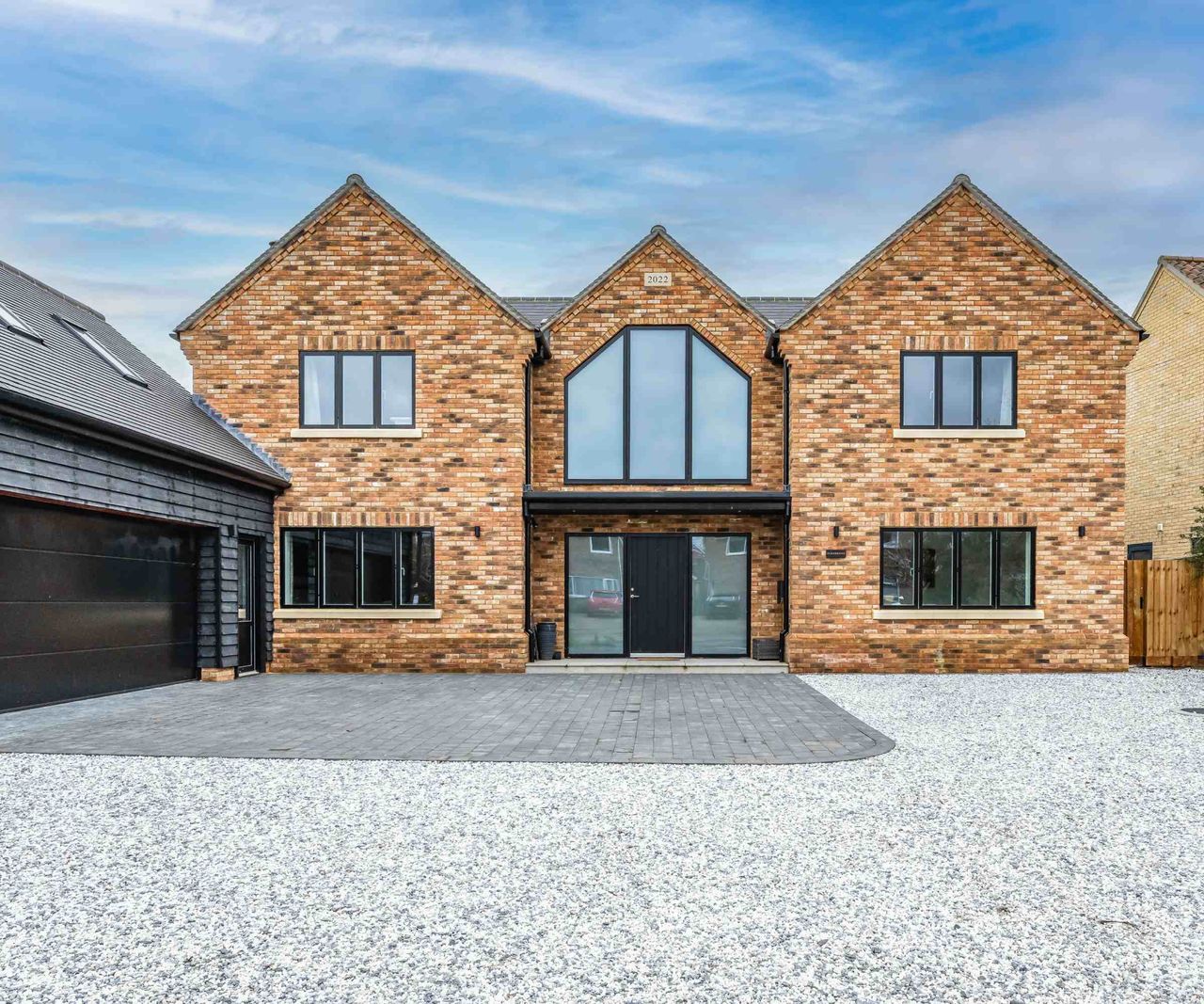 A brick-clad self build home with three prominent gable ends. The central gable features the front door and a large glazed focal window. The windows are from VELFAC. To the side is a large double garage.
