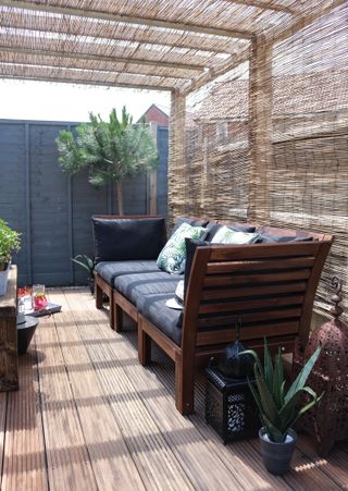 deck with black and wooden bench seat under a pergola, with potted plants dotted around
