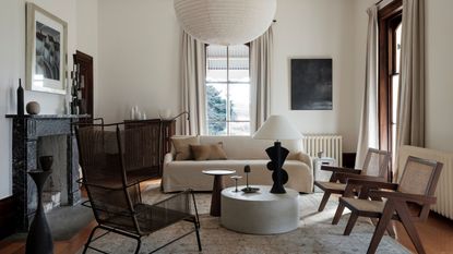 living room with white sofa, nesting coffee table with lamp, three armchairs, marble fireplace, curtains and large pendant light