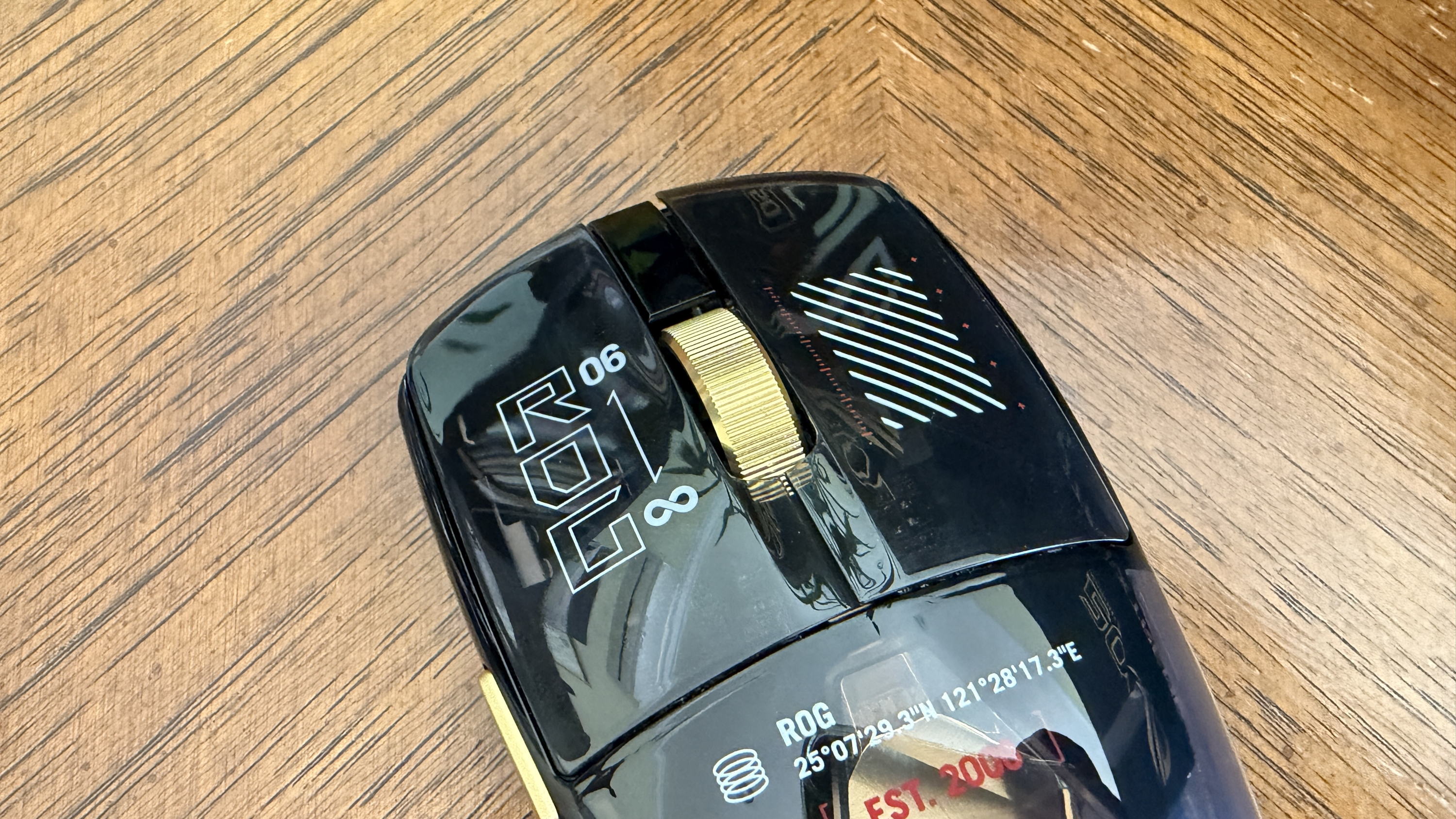 Black ASUS ROG computer mouse with gold scroll wheel on a wooden surface, featuring bold white text and designs.