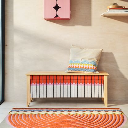 A patterned storage bench with a rug and a cushion from the IKEA OMMJ&Auml;NGE collection