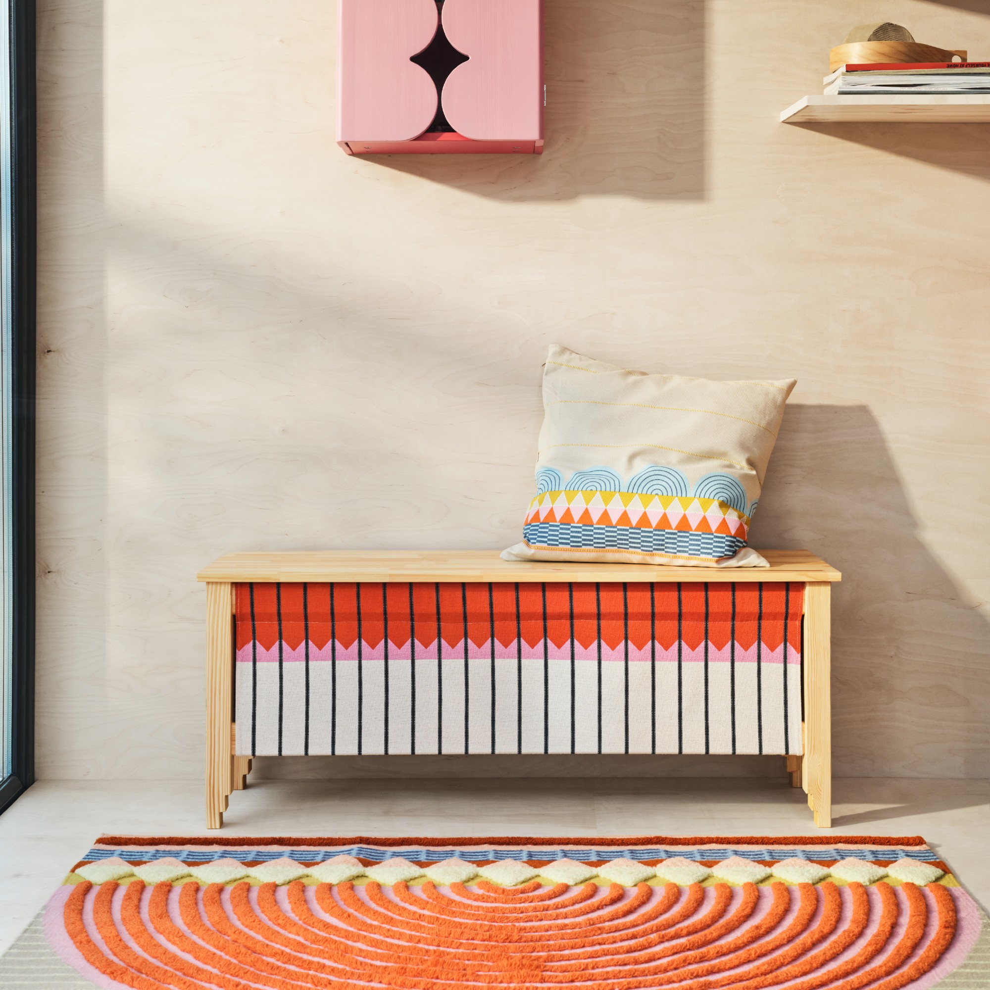 A patterned storage bench with a rug and a cushion from the IKEA OMMJÄNGE collection