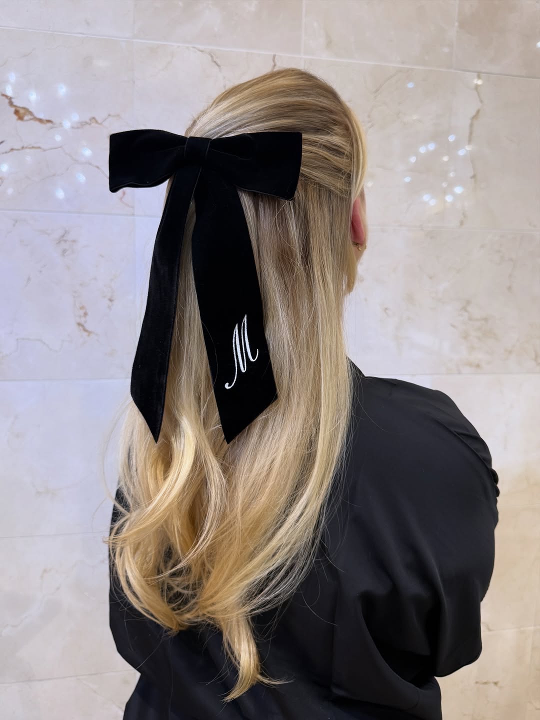 person with blonde hair wearing a large black monogramed velvet hair bow