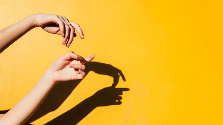 cropped hands gesturing against shadow on yellow background