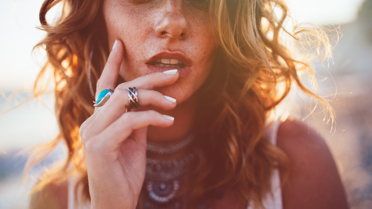 Close up of woman with auburn beach hair waves in her hair against a blurry background