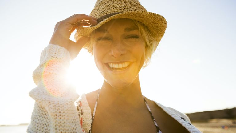 woman in hat on beach sun in background meant to symbolize summer solstice 2022