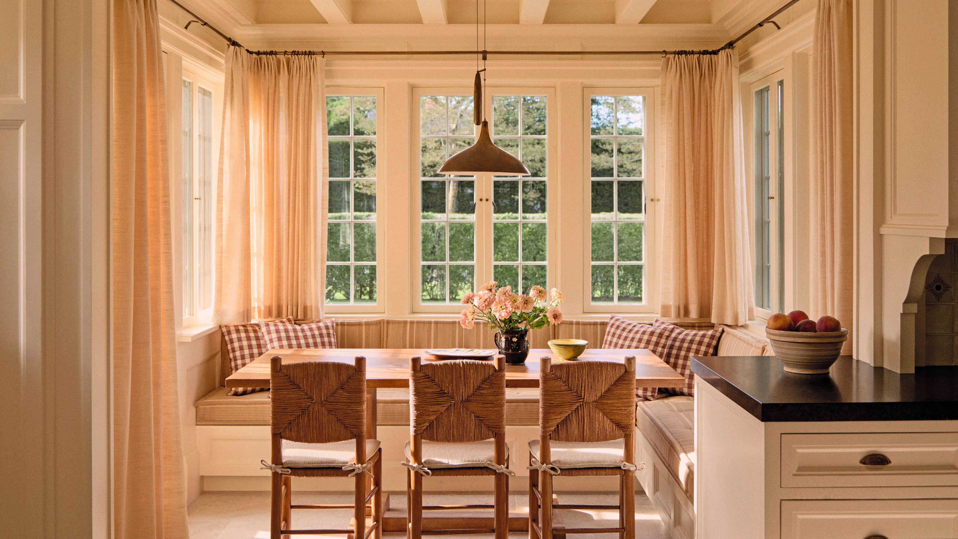 a large airy breakfast nook designed with coffered celing, french windows and a banquette seat with wooden table and woven chairs