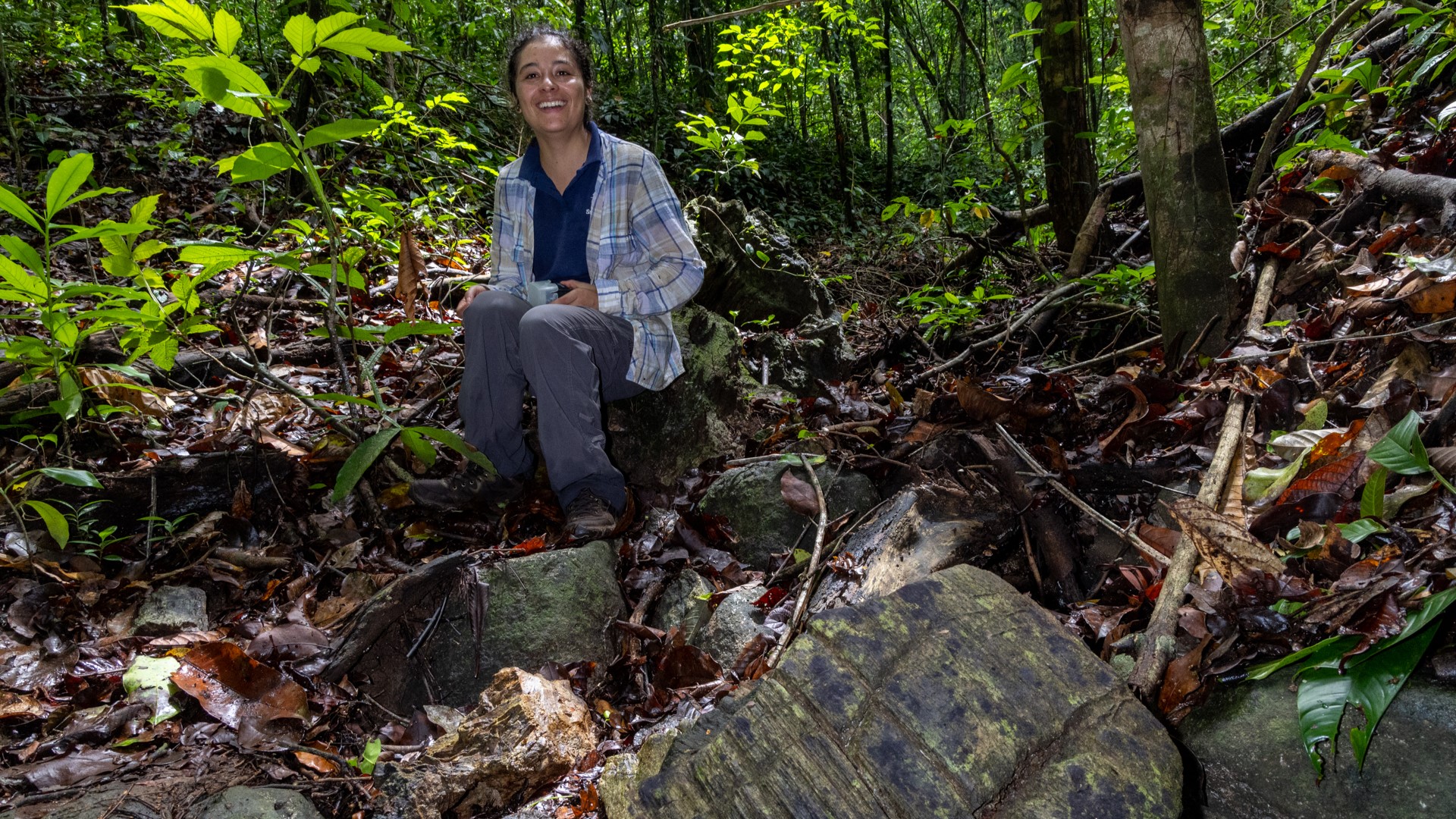 Researcher Camila Martínez Aguillón sits in the forest next to a fossilized wood sample.