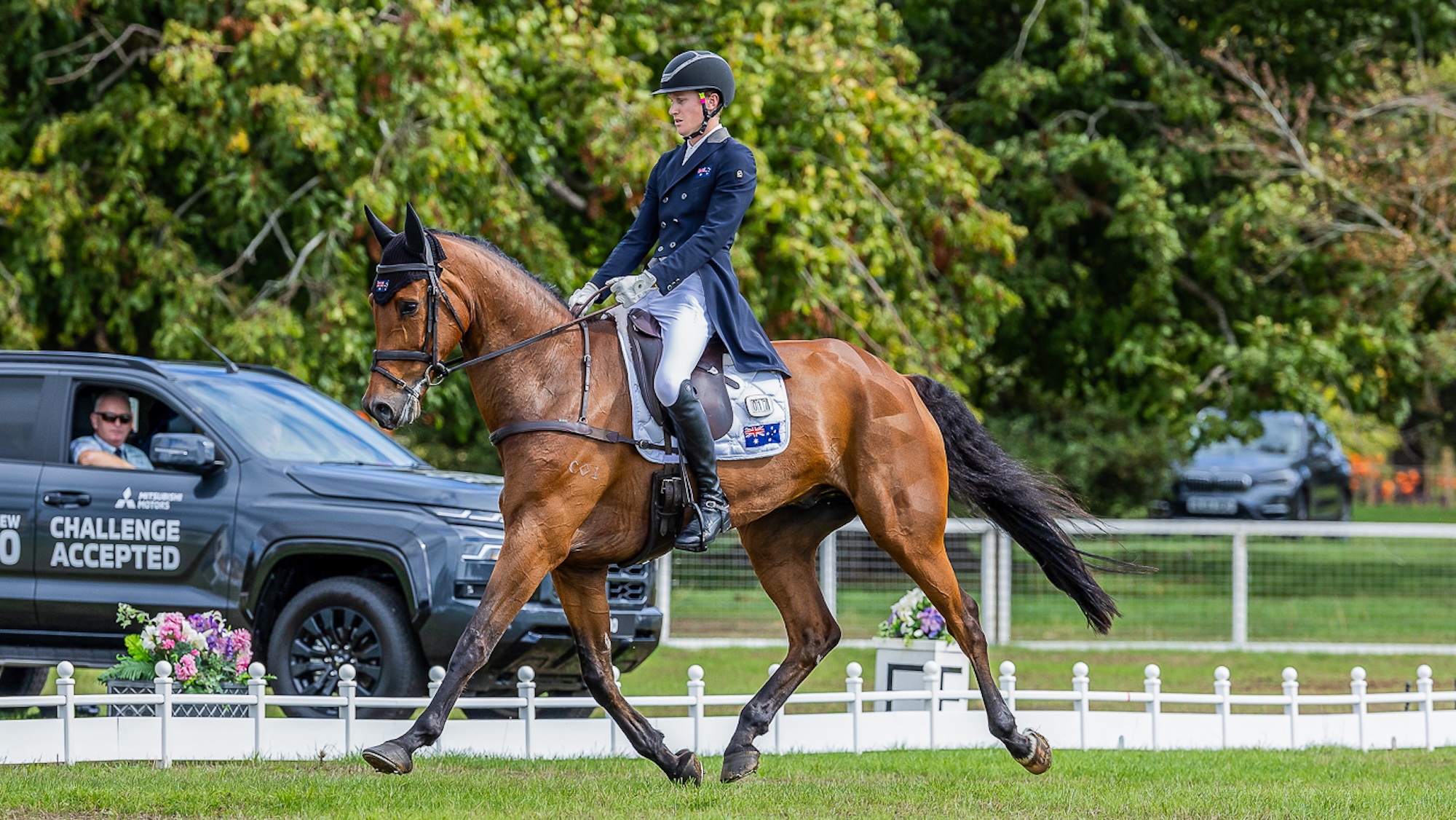 Oliver Barratt and Sandhills Briar, a rider in a blue tailcoat on a bay horse, trotting in the grass Blenheim Horse Trials dressage arena
