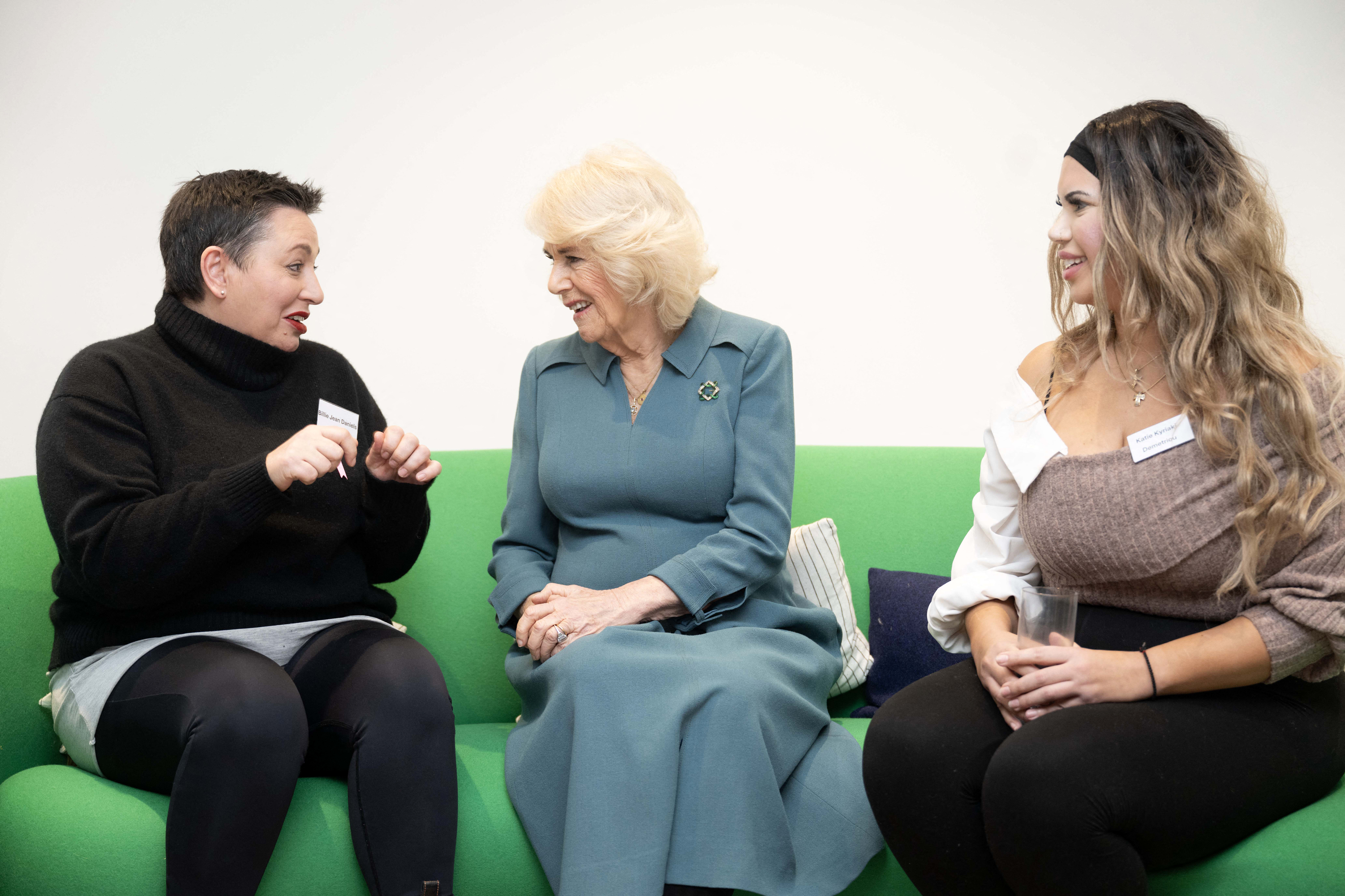 Queen Camilla sitting on a sofa talking to two ladies