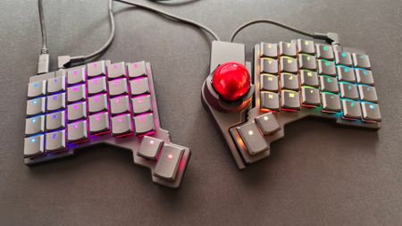 A photo of the ZSA Voyager ergonomic keyboard, with a ZSA Navigator trackball module attached to the right half