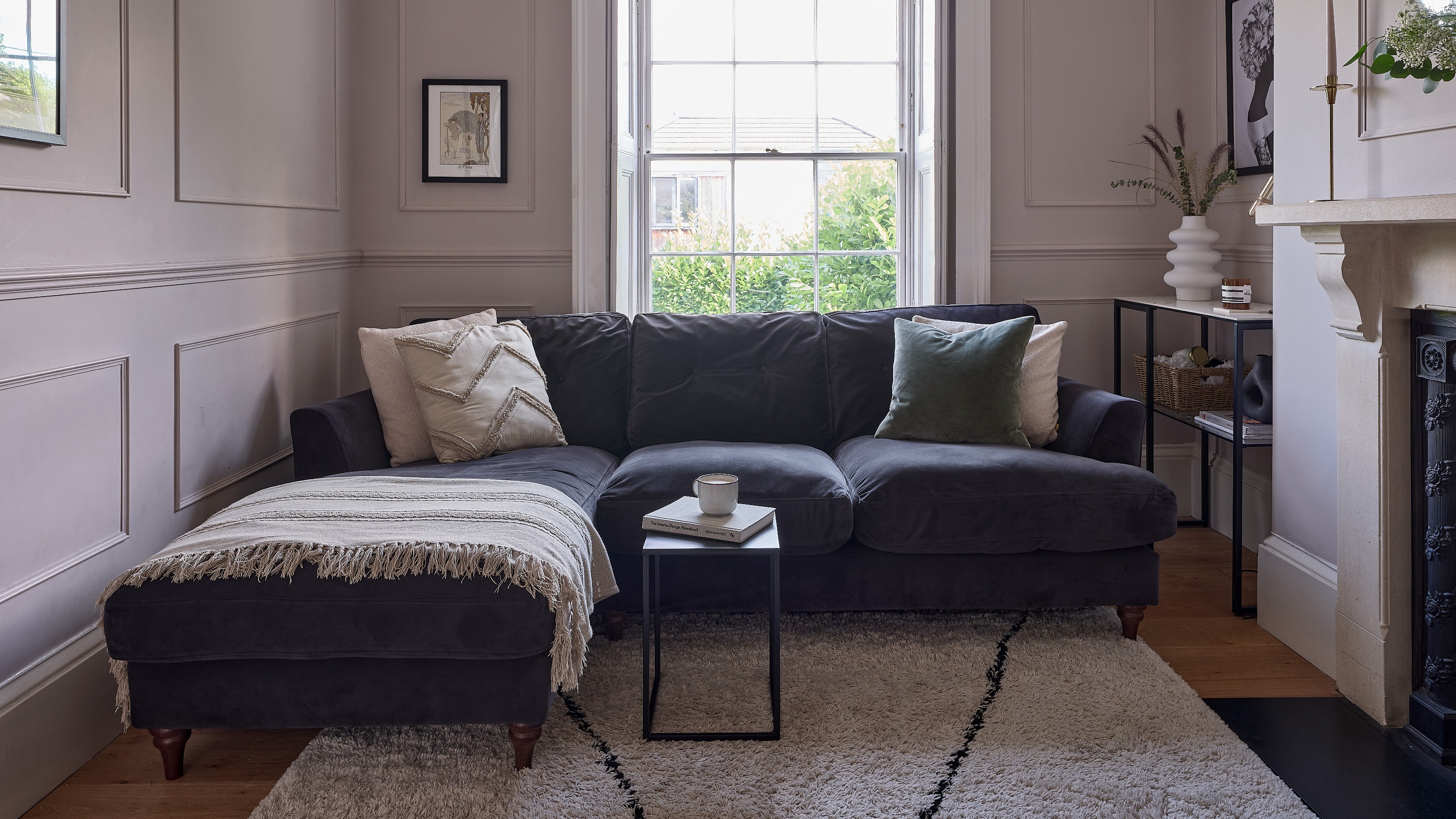 A narrow pink-painted living room with a chaise dark blue sofa and a Berber-style rug