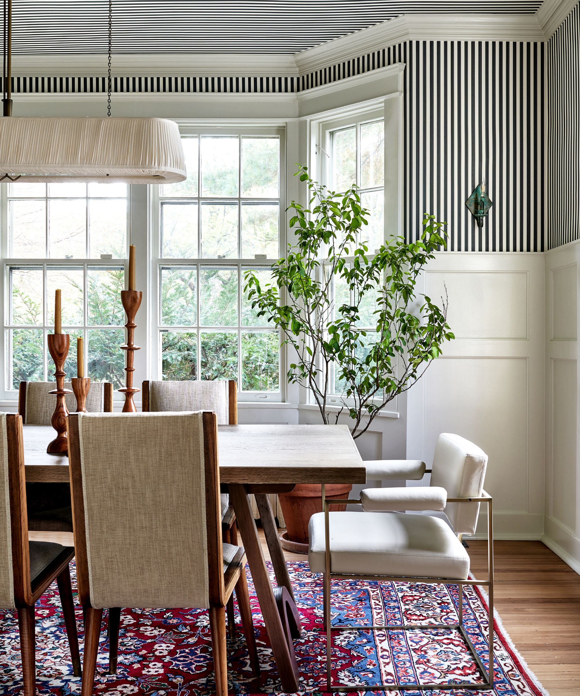 Dining room with striped wallpaper, crown molding, large bay windows, wooden dining table, modern table, wooden chairs and plant