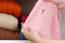 Person holding pink sweater with holes in in front of pile of folded sweaters iStock