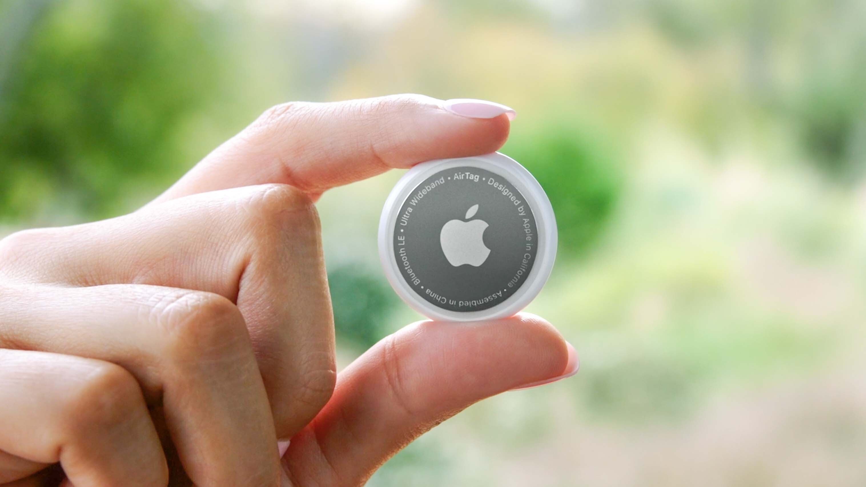 An Apple AirTag, held between a user's fingers in front of a blurred green background