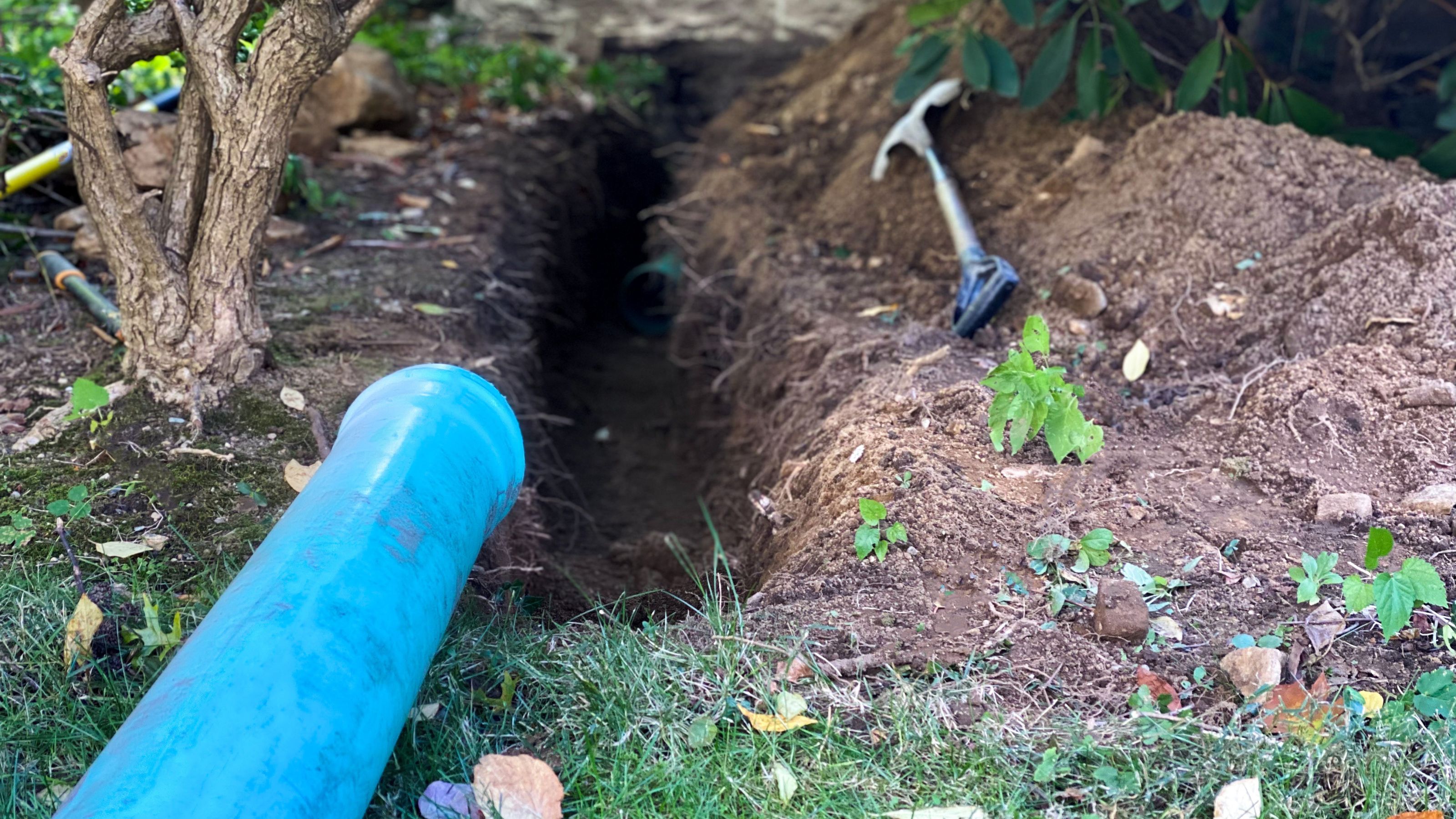 Spade and drainage pipe next to freshly-dug trench in garden