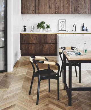 Kitchen flooring ideas illustrated by herringbone wood with black dining chairs.
