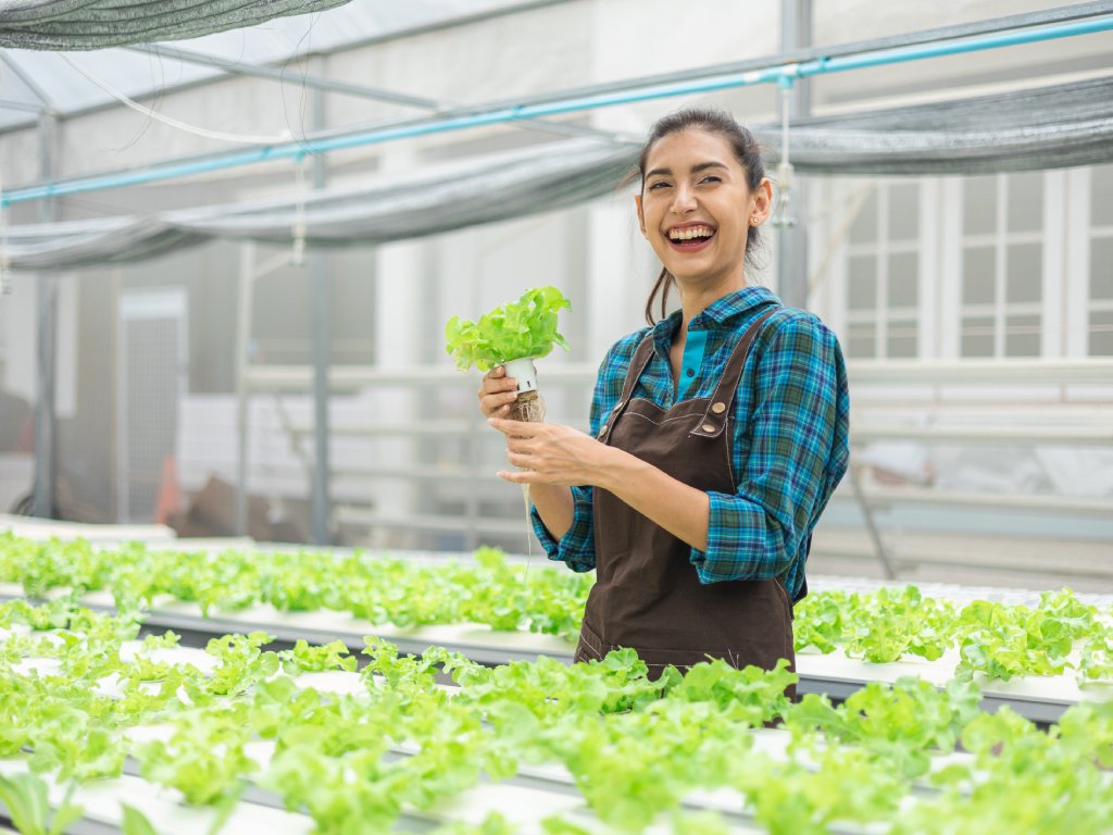 A smiling woman holds a lettuce plant in a hydroponic farm