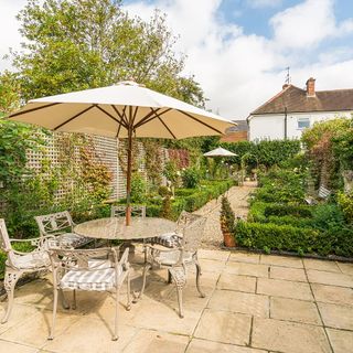 Garden table and chairs with white sun umbrella on pavers in green garden
