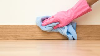 person wearing a pink glove cleaning skirting boards/base boards with a microfiber cloth