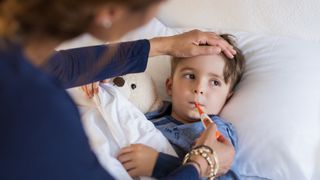 Mother checking temperature of her sick son who has thermometer in his mouth