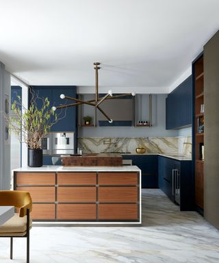 An example of modern kitchen lighting ideas showing a kitchen with a marble floor, dark blue cabinets and a wooden island
