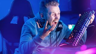 Angry computer gamer man yells and breaks keyboard 
