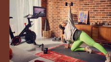 Woman using Peloton Bike+, down on yoga mat using weights in instructor-led strength training workout