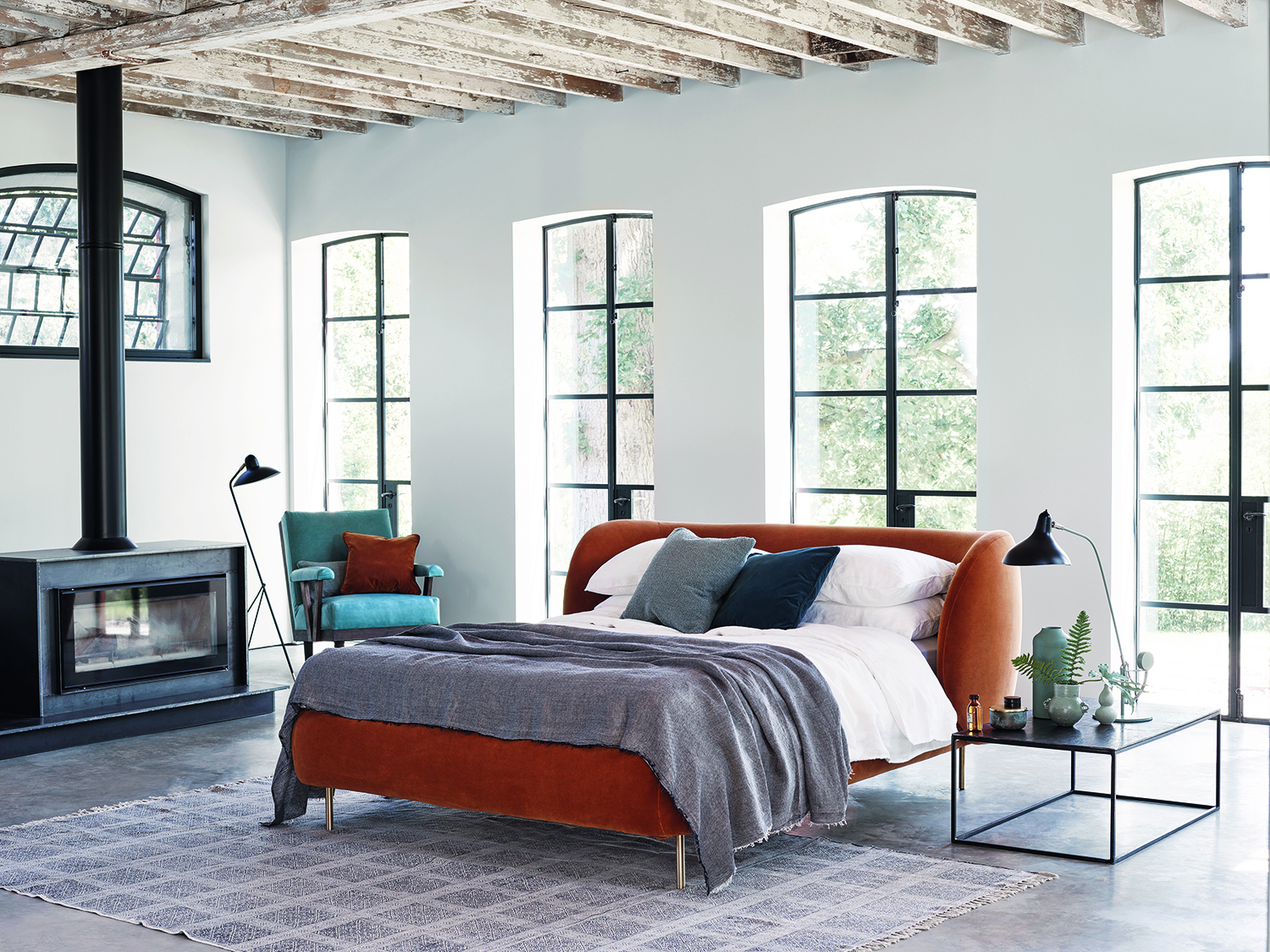 orange bed in white living room with large windows and a freestanding fireplace
